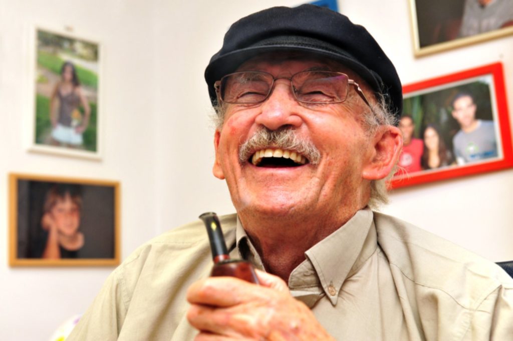 An older man laughing and holding a pipe