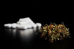 A pile of prescription drugs next to a pile of cannabis flower.