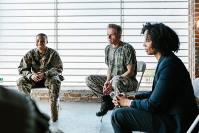 Soldiers in camo clothes sitting in chairs in a meeting.