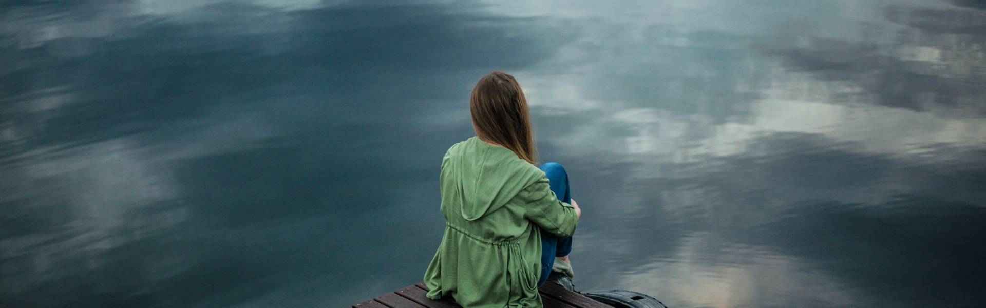 A woman sitting on a dock alone at a lake