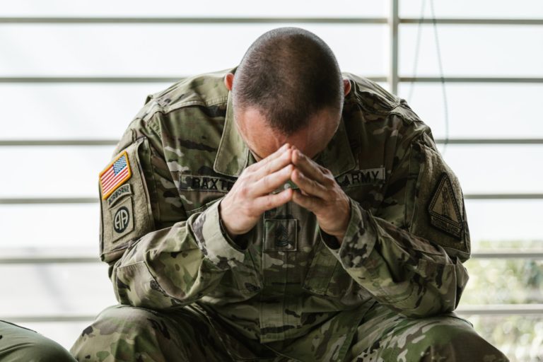 An American soldier sitting down and bowing his head.