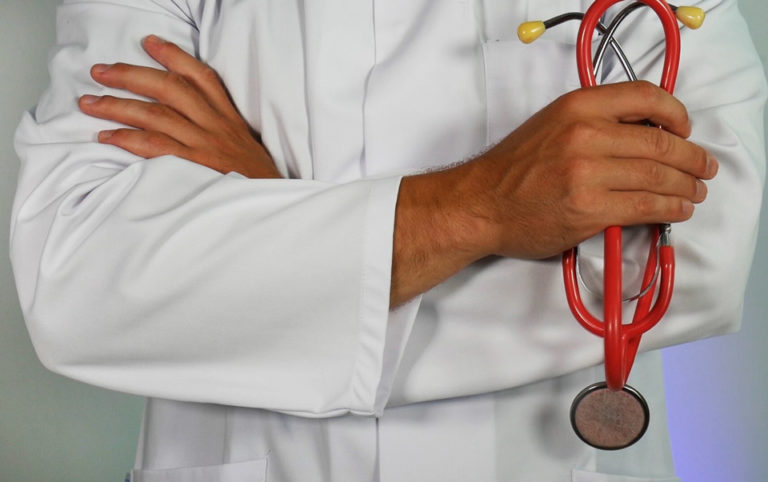 A doctor holding a stethoscope with his arms folded.