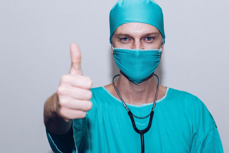 A masked nurse giving a thumbs up.