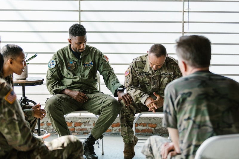 Veterans sitting together in a group with one man looking down and the other man touching his knee in support