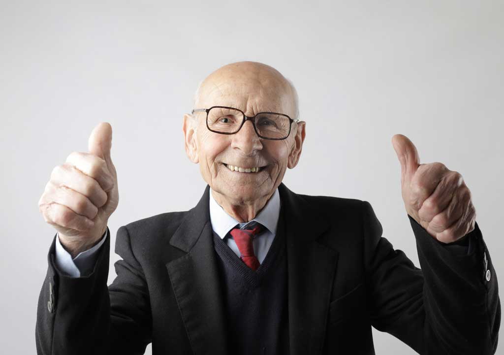 Old man smiling at the camera with two thumbs up