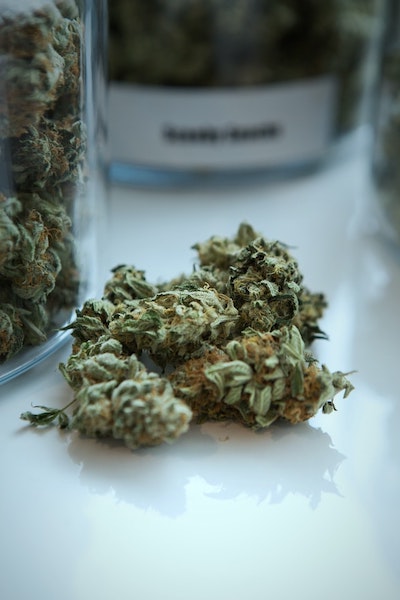 A pile of marijuana buds sitting on a table with multiple jars around them.