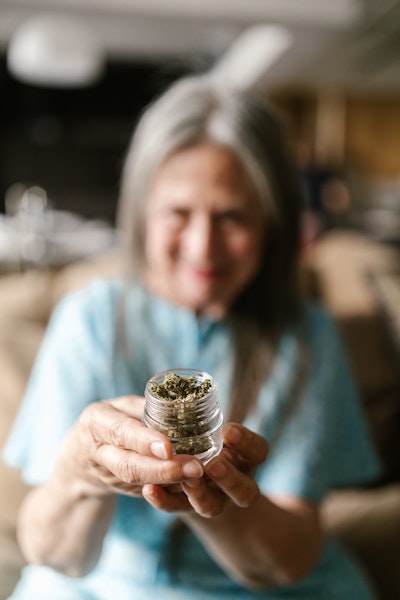 Woman in a blue hospital gown holding a small jar of medical marijuana. Filename: woman-holding-medical-marijuana
