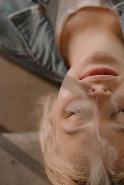 Woman laying down with her eyes closed and smoke wafting by her face.