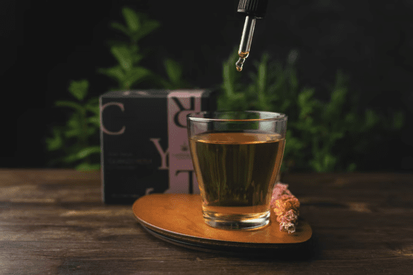 Dropper with tincture being added into a clear glass of tea