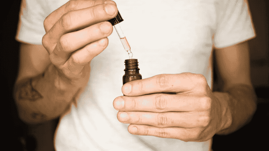 Man in white t-shirt holding dropper and vial with yellowish liquid