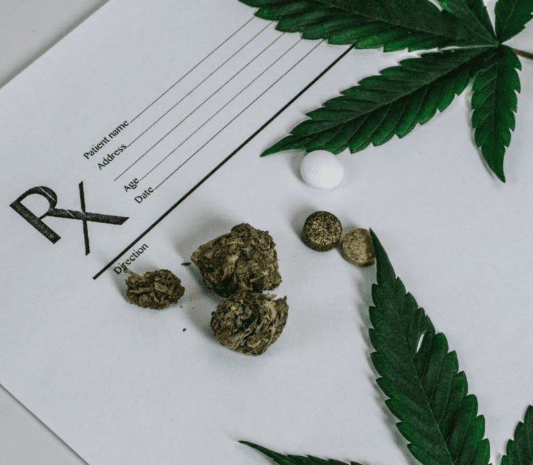 Dried marijuana and pills next to cannabis leaves on prescription pad