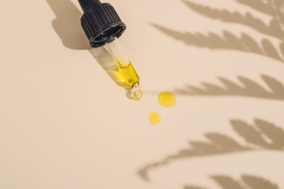 A dropper with tincture laying on a counter with some drops of liquid and the shadow of a marijuana plant