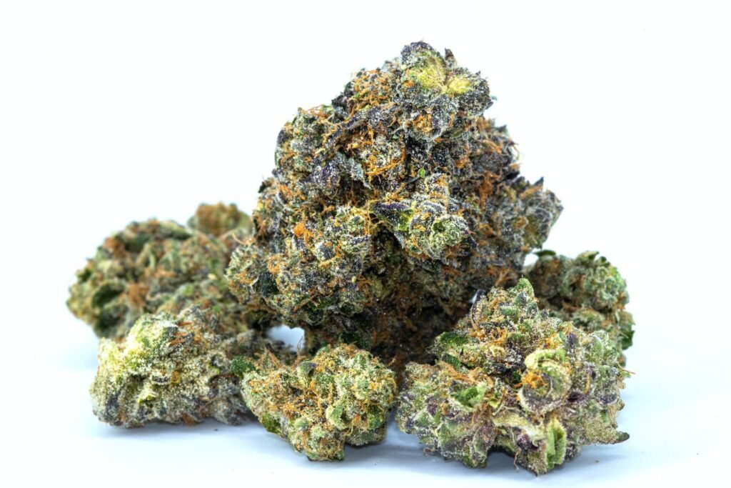 A premium, frosty clumps of dried cannabis buds featuring dense purple tones, bright orange hairs, and a heavy coating of trichomes against a clean white background.
