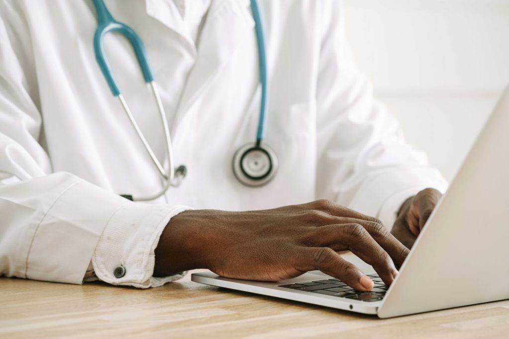 Doctor in lab coat typing on laptop, face obscured