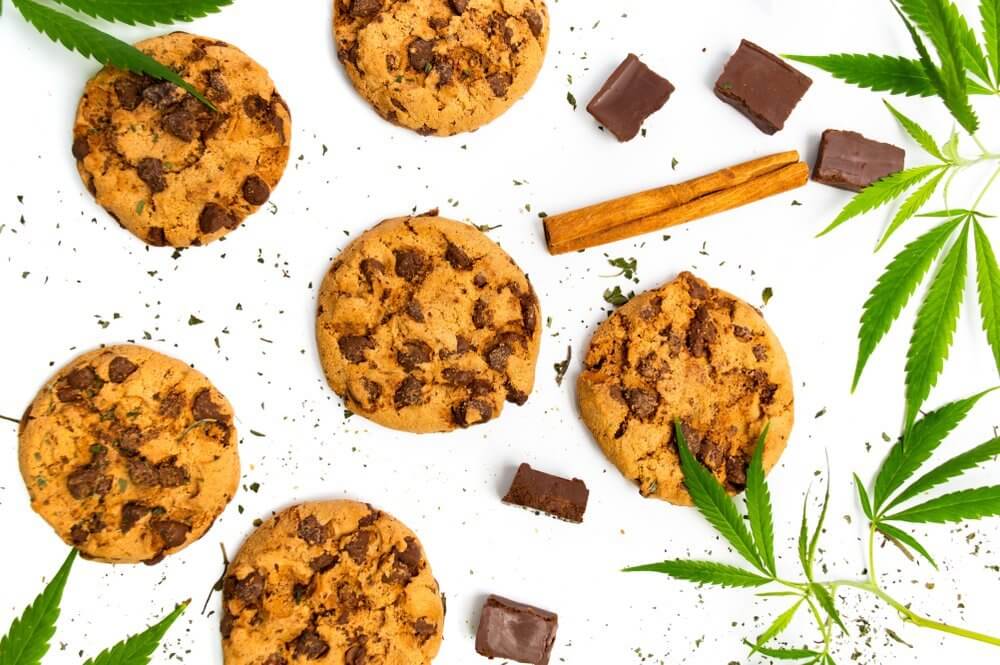 Cannabis chocolate chip cookie edibles and marijuana leaves on a table