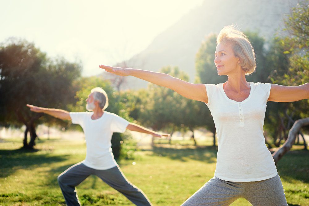 Man and woman doing yoga stretches at the park on a sunny day