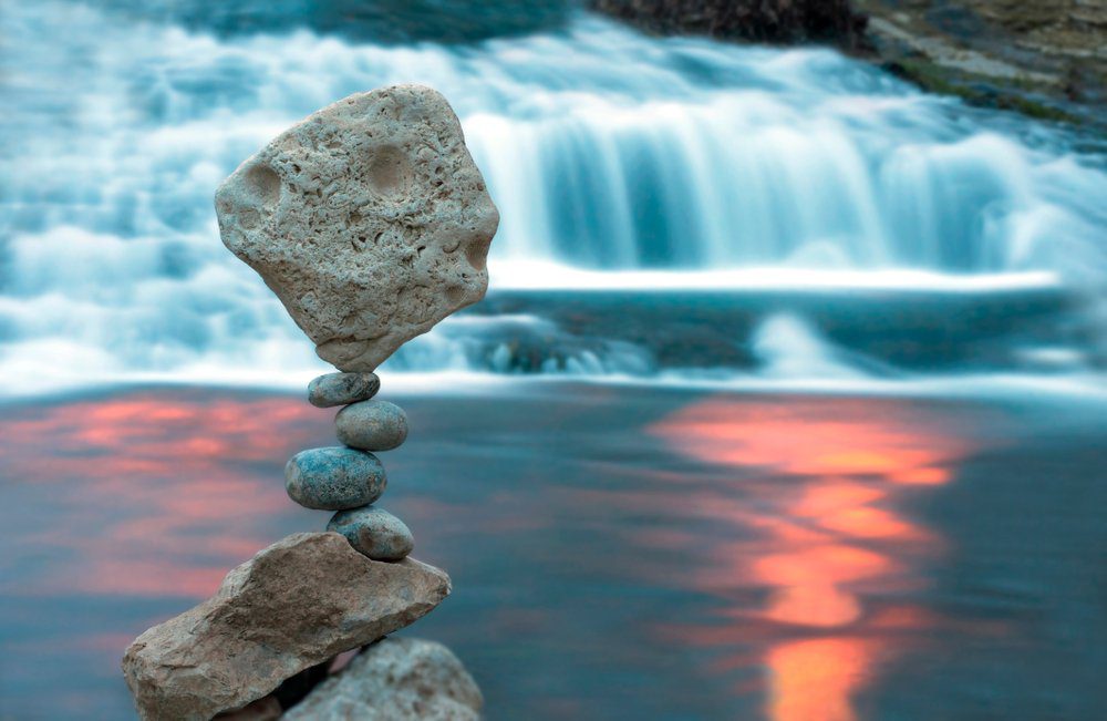 Balancing rocks stacked against a body of water with a waterfall in the background
