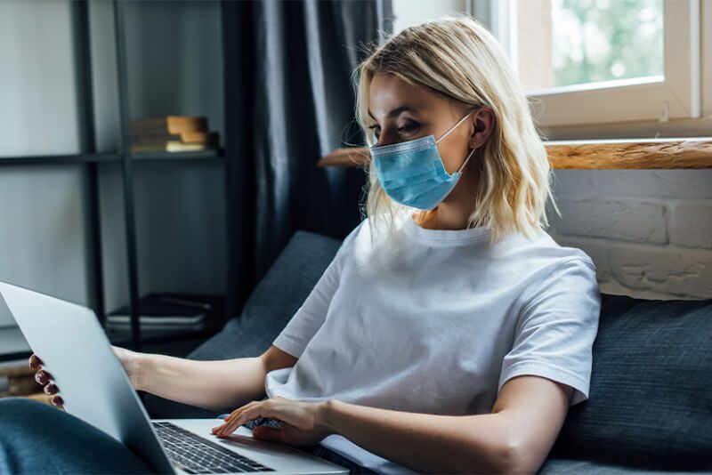 young woman in medical mask using laptop at home