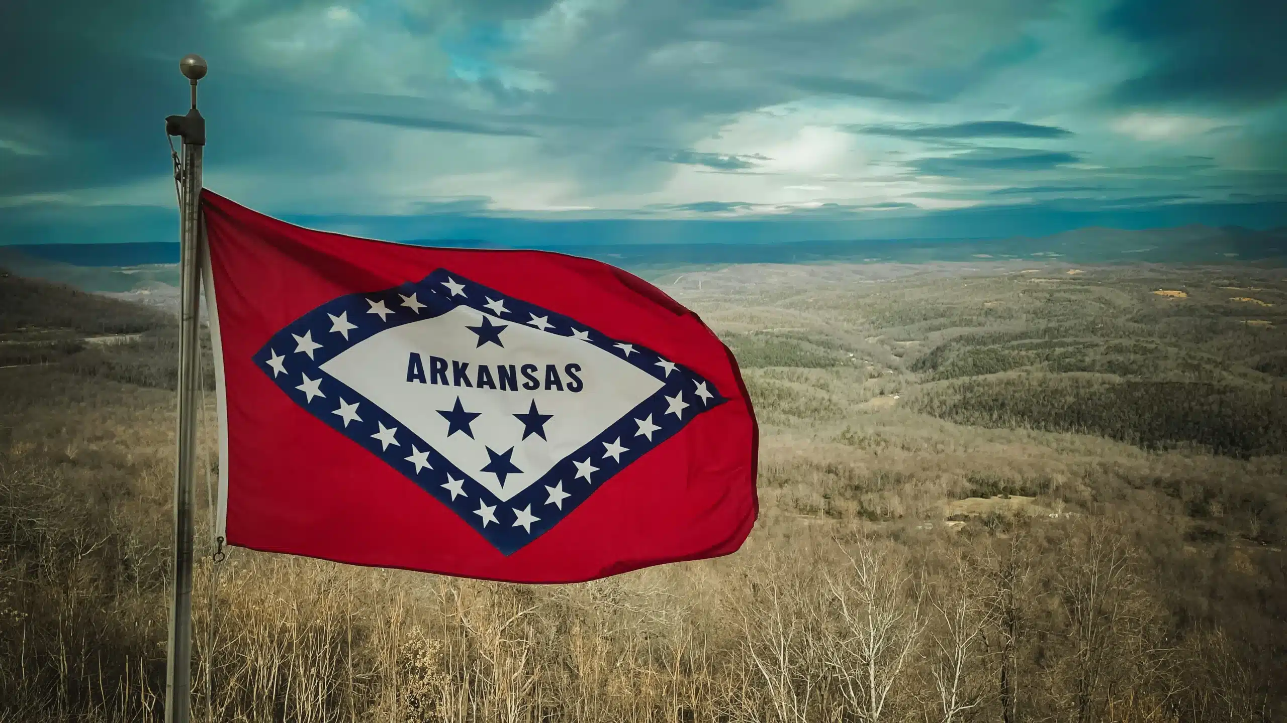 Arkansas state flag waving over scenic hills, representing the current state of MMJ in Arkansas.